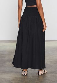 Jupe maxi smockée noire avec une coupe A-line fluide, tissu texturé, associée à des chaussures perforées à bout ouvert.