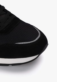 Zapatilla negra con una mezcla de malla texturizada y materiales de ante. Detalles curvados blancos en la suela exterior con una gruesa suela de goma negra.