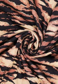 Tessuto lavorato a maglia con un design a spirale, caratterizzato da un motivo a strisce di tigre nei colori nero, beige e accenti metallici dorati. Texture morbida.