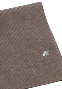 Bonnet en tricot marron avec une texture côtelée et un logo argenté cousu. Le tissu semble doux et élastique, adapté aux temps froids.