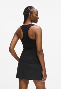 Μαύρο, ριγωτό μπλουζάκι με ράντερ σχεδίαση, συνδυασμένο με μια μαύρη φούστα. Η λεία υφή και η εφαρμοστή σιλουέτα ενισχύουν μια αθλητική εμφάνιση.