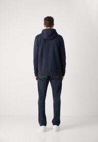 Navyblauwe hoodie met een gladde textuur, gecombineerd met donkere jeans en witte sneakers. Het ontwerp toont een achteraanzicht.