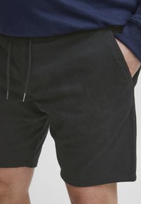 Pantalones cortos de algodón negros con bolsillos laterales y cierre de cordón. Textura suave, longitud a medio muslo y un diseño casual.