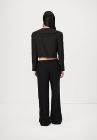 Blazer noir coupé avec des revers larges, des épaules structurées et des poignets ajustés, associé à un pantalon noir à taille haute et à jambes larges.