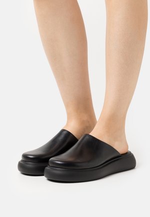 Zuecos de piel negra con un acabado suave y una abertura amplia. Suela elevada y redondeada que ofrece un aspecto moderno y cómodo.