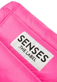 Rosa gestepptes Gewebe mit einem weißen Etikett, auf dem in schwarzer Schrift "SENSES .THE LABEL" steht, das Nähdetails und eine glatte Textur zeigt.