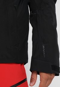 Schwarze wasserdichte Jackenärmel mit elastischem Bündchen und Klettverschluss. Mit "DRYVENT®"-Branding nahe dem Bündchen. Glatte, matte Textur.