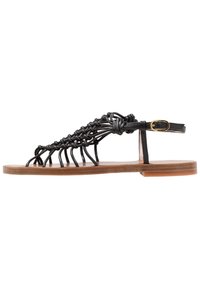 Sandale en cuir noir avec des lanières tressées complexes, un design à bout ouvert, une fermeture à boucle autour de la cheville et une semelle plate marron.