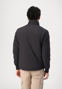 Black puffer jacket with a high collar, elastic cuffs, and a smooth, matte finish. Features a streamlined design and minimalistic style.