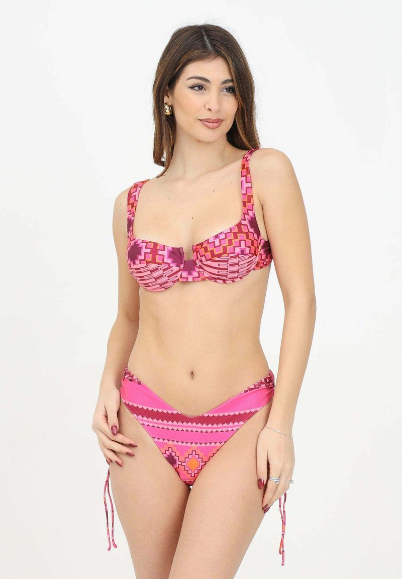 Bikini a due pezzi con un motivo geometrico rosa, dotato di coppe morbide e lacci regolabili sui lati della parte inferiore. Texture morbida.