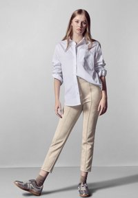 Witte overhemd met opgerolde mouwen, beige op maat gemaakte broek met zijstiksels, en gestreepte grijze sneakers met bruine accenten.