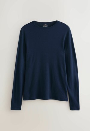 Tumši zils, garām piedurknēm krekls ar apaļu kakla izgriezumu, izgatavots no mīkstas, elastīgas auduma. Vienkāršs dizains bez redzamām rakstu zīmēm vai akcentiem.