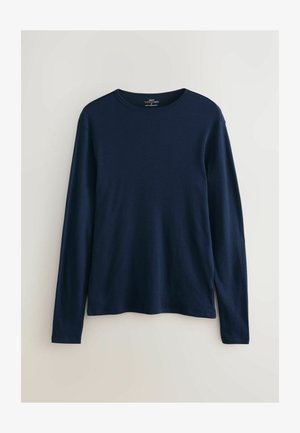 Tumši zils, garām piedurknēm krekls ar apaļu kakla izgriezumu, izgatavots no mīkstas, elastīgas auduma. Vienkāršs dizains bez redzamām rakstu zīmēm vai akcentiem.