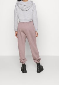 Sudadera gris corta con mangas largas, combinada con joggers rosas con puños elásticos, llevada con botas negras de suela gruesa.