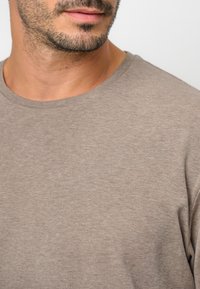 Brązowy T-shirt z okrągłym dekoltem, wykonany z miękkiej bawełnianej tkaniny, charakteryzujący się gładką fakturą oraz prostym, casualowym designem bez wzorów i dodatków.