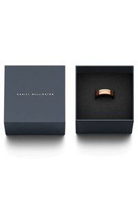 Rose gold -värinen metallisormus, jonka sisäpuolella on kaiverrettu logo, tummansinisessä rasia, jossa on pehmeä musta sisustus ja minimalistinen muotoilu.