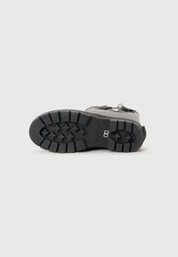Black boot lying on its side showing a rugged sole with deep treads and size label "5" on a plain light background.