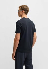 Svart kortärmad t-shirt i mjukt tyg, med rund halsringning och en diskret detalj på ryggen, kombinerad med mörka träningsbyxor.