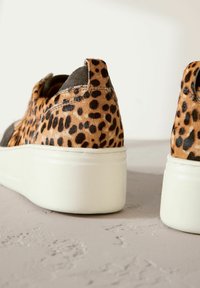 Leopard-print sneaker with a textured fur upper, grey accents, and a white platform sole. Features a back pull tab for easy wear.