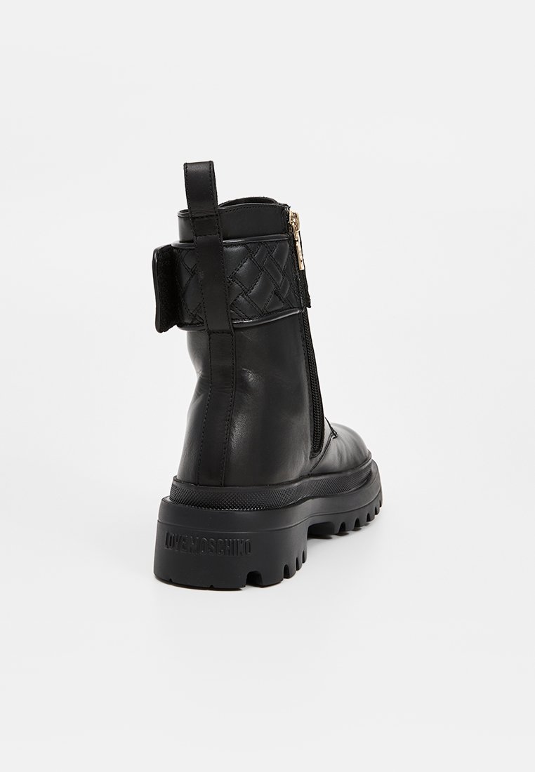 Stivaletto alla caviglia in pelle nera con suola spessa, chiusura a zip e dettaglio intrecciato nella parte superiore. Marchio visibile sul tallone. Finitura opaca.