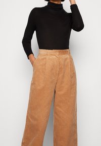 Svart polotröja kombinerad med tanfärgade kordflöjtbyxor med vida ben, vertikala ränder, hög midja och framfickor.