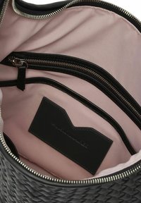 Interno della borsa in pelle intrecciata nera con fodera rosa chiaro, una tasca con zip e un'etichetta in pelle nera con logo. Hardware della zip visibile.