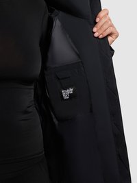 Svart kviltad jacka med en slät inredning, med en sidoficka som har en etikett. Ytan har en elegant, matt finish och minimala detaljer.