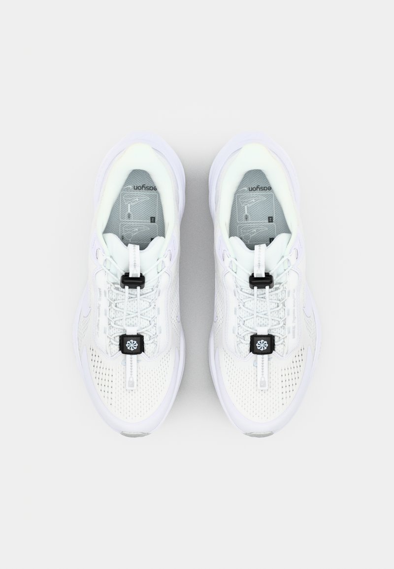 Zapatillas deportivas blancas con parte superior de malla, cordones texturizados y un cierre de toggle negro. Cuentan con una suela acolchada y un diseño elegante y curvado.