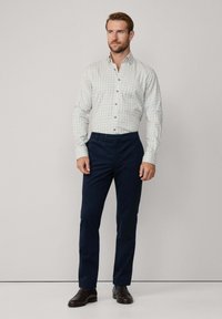 Overhemd met knoopsluiting in een groen en blauwe ruitpatroon, gecombineerd met marineblauwe gepaste broek. Bruine leren schoenen maken de outfit af.