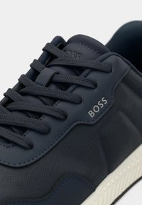 Baskets bleu marine en matériau texturé, design à lacets, semelle en caoutchouc blanche et logo embossé sur le côté. Caractérisées par des accents contrastants.