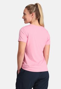 Helles rosa T-Shirt mit kurzen Ärmeln, aus weichem, dehnbarem Stoff, mit einem runden Halsausschnitt und einer körpernahen Silhouette. Getragen mit dunklen Hosen.
