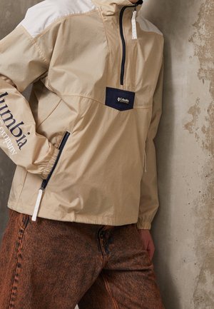 Chaqueta de pullover beige con un bolsillo en el pecho de color marino y acentos blancos en los hombros. Cuenta con cierre de cremallera, puños elásticos y logotipo en la manga.