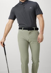 Black and gray striped polo shirt with short sleeves, paired with light green pants and a black woven belt. Golf club held in left hand.