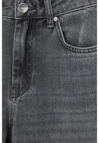 Gros plan d'un jean en denim gris foncé montrant la poche avant, la passants de ceinture et le bouton métallique avec la marque "PULL&BEAR".