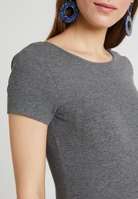 Gray ribbed short-sleeve top with a round neckline, featuring a fitted design. Worn with blue circular earrings for added detail.
