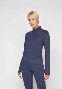 Dunkelblaues Sportjacke aus strukturiertem Stoff, mit hohem Kragen, durchgehendem Reißverschluss und langen Ärmeln, kombiniert mit passenden, eng anliegenden Leggings.