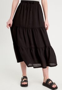 Falda negra de capas hecha de un tejido ligero. Cuenta con una cintura elástica y una silueta fluida, combinada con sandalias planas negras con tachuelas.