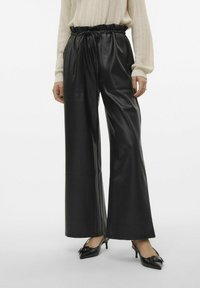 Zwarte faux leren broek met wijde pijpen, voorzien van een elastische tailleband en een trekkoord, met twee voorzakken, gecombineerd met zwarte hakken.