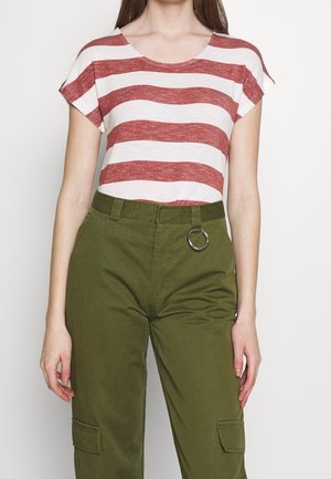 Femme portant un haut à rayures rouges et blanches à manches courtes rentré dans un pantalon cargo olive taille haute avec un détail en anneau métallique.