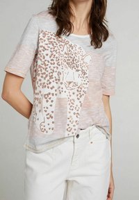 Camiseta gris claro con un diseño de leopardo en detalles metálicos color rosa dorado, de manga corta y corte relajado. Pantalones de algodón blancos mostrados.