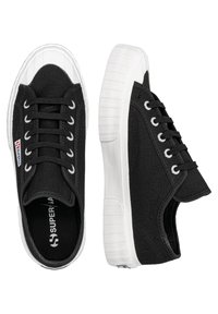 Sneaker in tela nera con punta e suola in gomma bianca, caratterizzati da occhielli in metallo e lacci. Il design è a profilo basso e leggero.