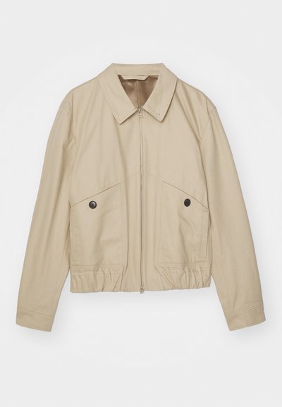 Beige lightweight jacket with a pointed collar, front zipper, two large pockets, and elastic waist. Smooth texture with a minimalist design.