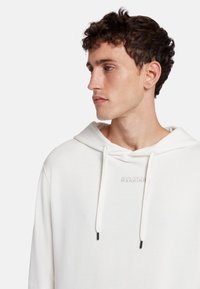 Felpa bianca con cappuccio e coulisse, caratterizzata da un logo discreto sul petto. Tessuto morbido, vestibilità comoda, senza motivi o dettagli visibili.