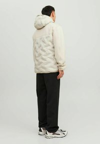 Padded hooded jacket šviesiai bežinėje spalvoje, su tekstūruotu siuvinėtu nugara. Derinama su laisvais juodais kelnėmis ir kedais su sidabro akcentais.