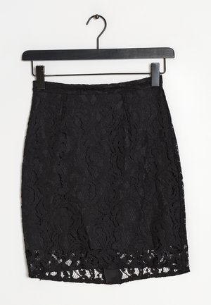 Falda de encaje negro con un intrincado patrón floral, con un diseño ajustado y dobladillo de encaje con bordes en forma de ondas. Colgada en una percha de metal negro.