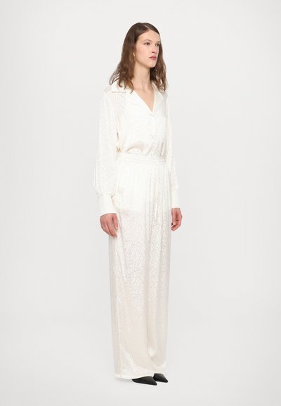 White, textured long dress with a collar and elastic waist. Features slightly puffed long sleeves and a relaxed fit, paired with black shoes.