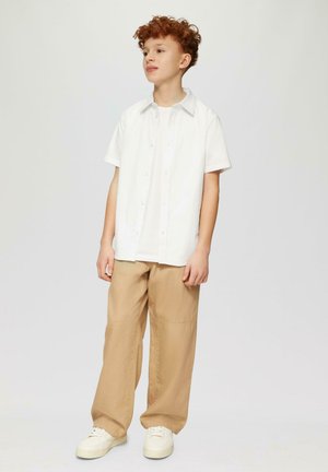 Weißes Kurzarmhemd mit Knopfleiste, kombiniert mit beigeweiten Hosen und weißen Turnschuhen, die eine entspannte Passform und eine glatte Textur zeigen.