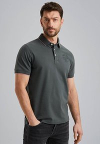 Polo gris avec un col et deux boutons, arborant un logo subtil, des accents roses contrastants sur le col et les manches. Matière en coton.