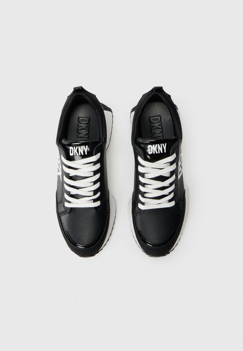 Baskets synthétiques noires avec des lacets blancs et une marque DKNY. Tige texturée, pointe arrondie et semelle blanche contrastante.