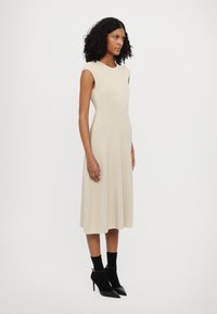 Beige ribbed dress with cap sleeves, fitted bodice, and a flared skirt. Paired with black high-heeled shoes and ankle socks.